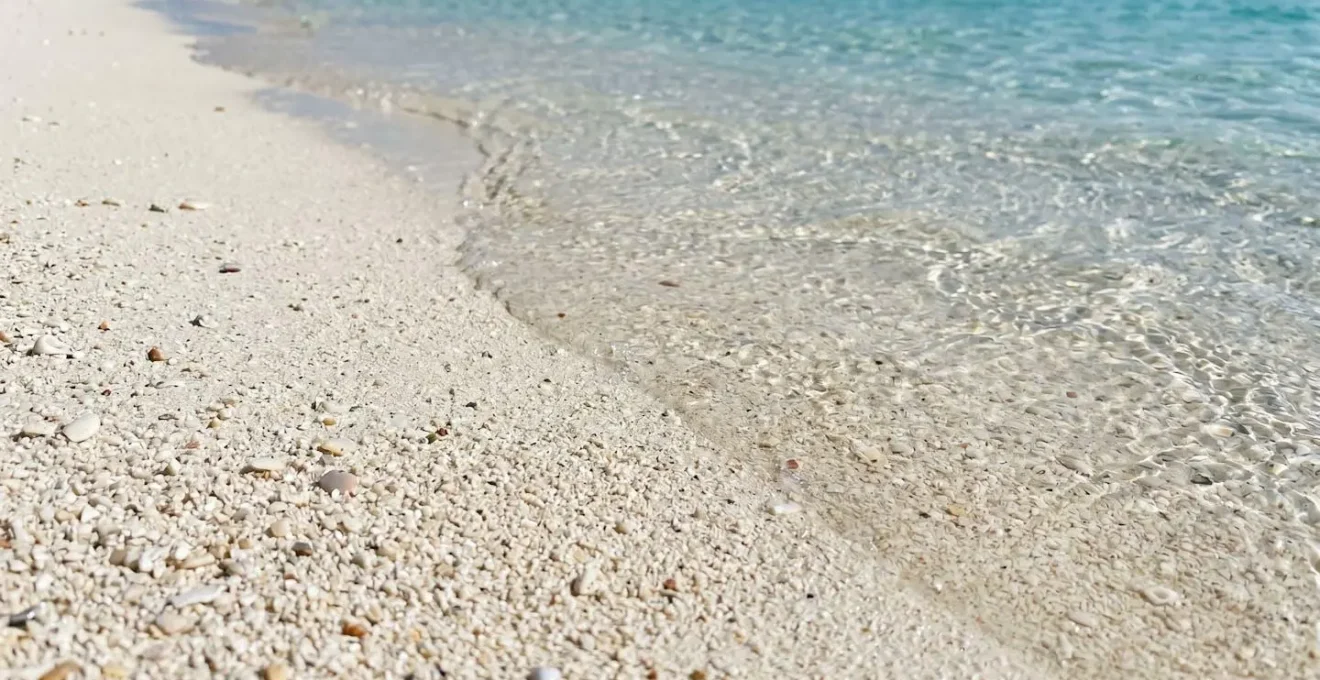 Gros plan sur du sable blanc fin rencontrant une eau turquoise cristalline, avec un effet bokeh en arrière-plan