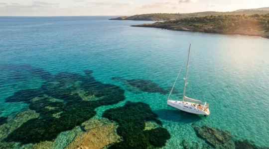 Bateau naviguant dans les eaux turquoise de la Méditerranée française au-dessus d'un herbier de posidonie visible sous l'eau
