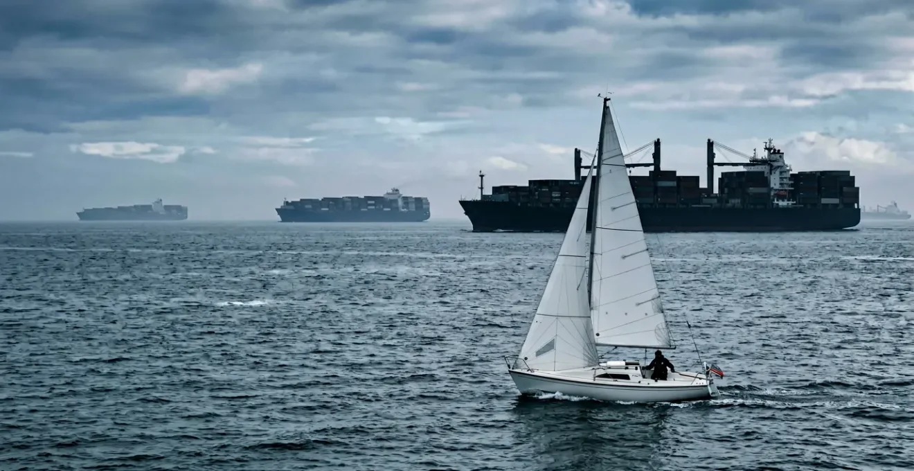 Petit voilier traversant un dispositif de séparation du trafic maritime avec grands navires cargo en arrière-plan