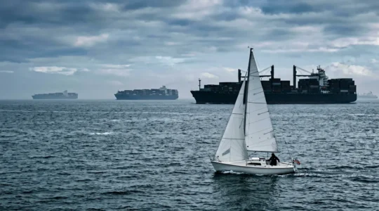 Petit voilier traversant un dispositif de séparation du trafic maritime avec grands navires cargo en arrière-plan
