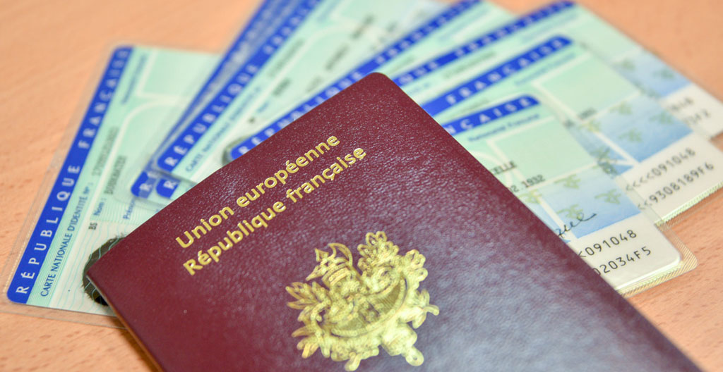 Gros plan sur des mains tenant des billets de ferry et passeports sur une table en bois clair, avec un flou artistique en arrière-plan